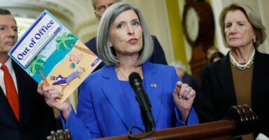 Senator Joni Ernst in a blue suitIn front of a podium and microphone speaking to the media