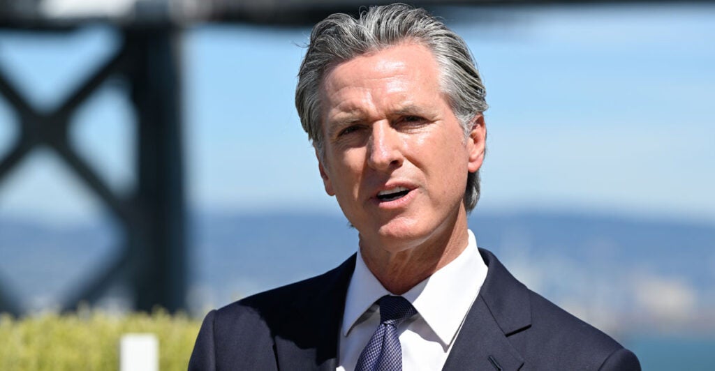 Newsom speaks to the press in front of a California valley view.