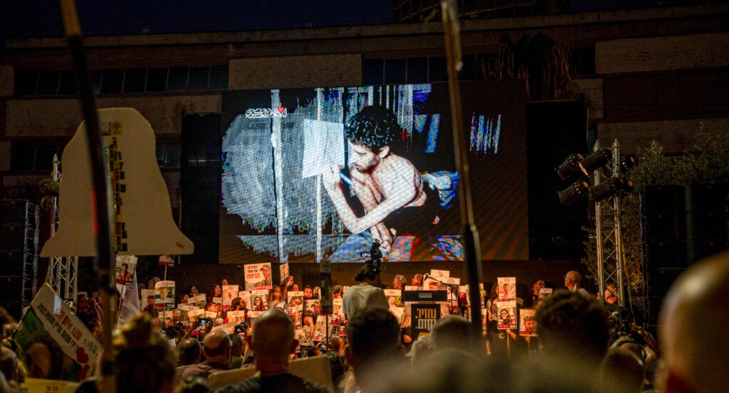 Footage of the Israeli hostage is displayed on a larger screen, with hundreds of people gathering around to show support for the hostage's family.