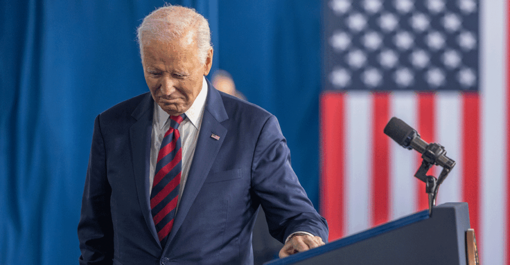 Joe Biden in a suit looks down as he walks away from a podium