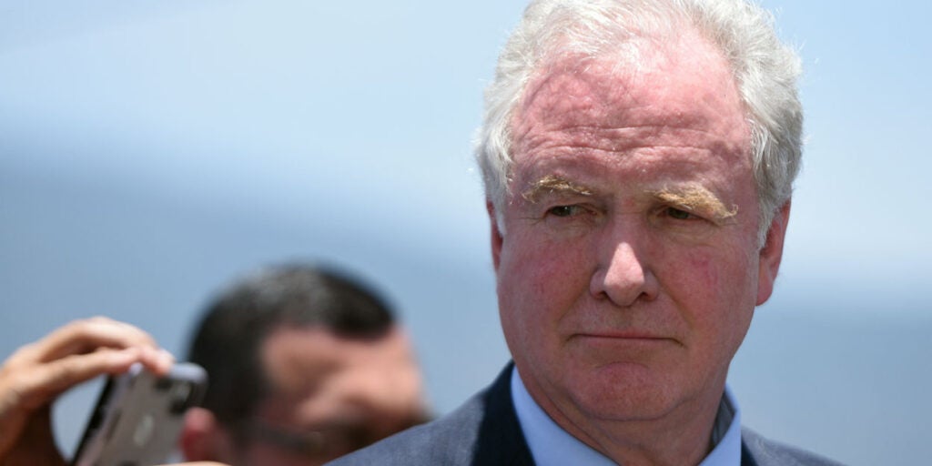 A close-up photo shows Sen. Chris Van Hollen looking on during a press conference.