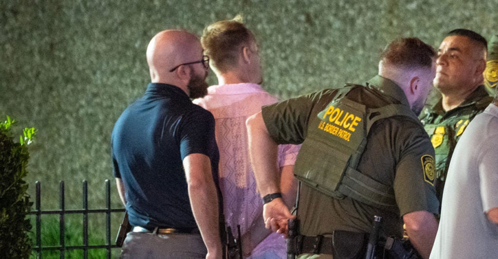 The suspect, a middle aged man in a pink shirt, is handcuffed by officers.