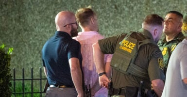 The suspect, a middle aged man in a pink shirt, is handcuffed by officers.