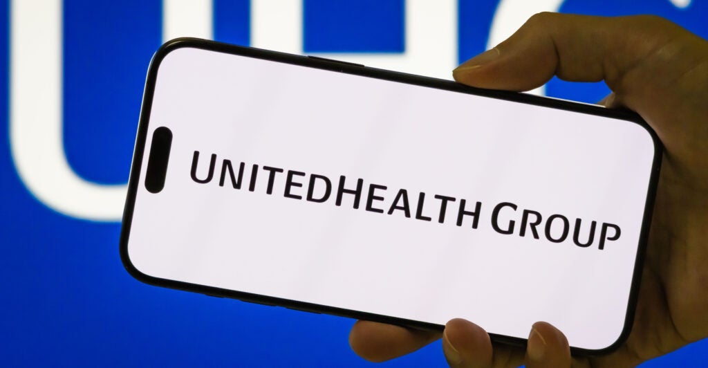 In this photo illustration, a person holds a smartphone displaying the logo of UnitedHealth Group Incorporated (NYSE: UNH), a leading American healthcare and insurance company, with the company's blue UHG branding visible in the background, on July 27, 2025 in Chongqing, China.