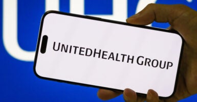 In this photo illustration, a person holds a smartphone displaying the logo of UnitedHealth Group Incorporated (NYSE: UNH), a leading American healthcare and insurance company, with the company's blue UHG branding visible in the background, on July 27, 2025 in Chongqing, China.