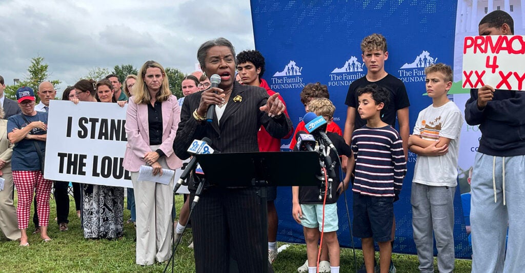 Winsome Earle-Sears in front of a sign reading "I Stand With The Loudoun 3"