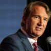 Virginia Gov. Glenn Youngkin in a dark suit on a stage speaking into a microphone