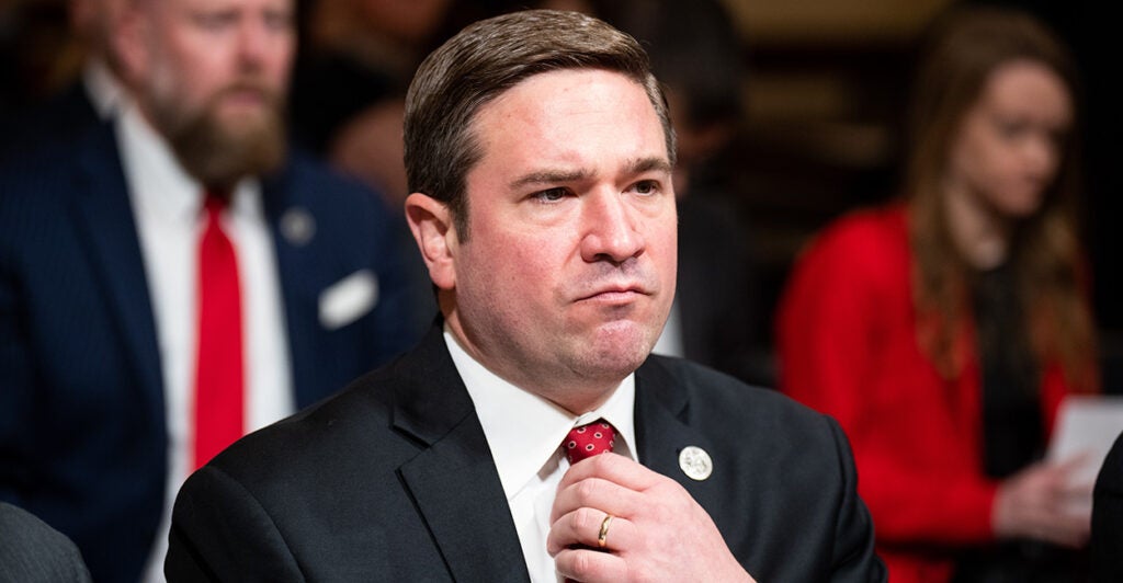 Missouri Attorney General Andrew Bailey adjusts his tie while sitting at a hearing
