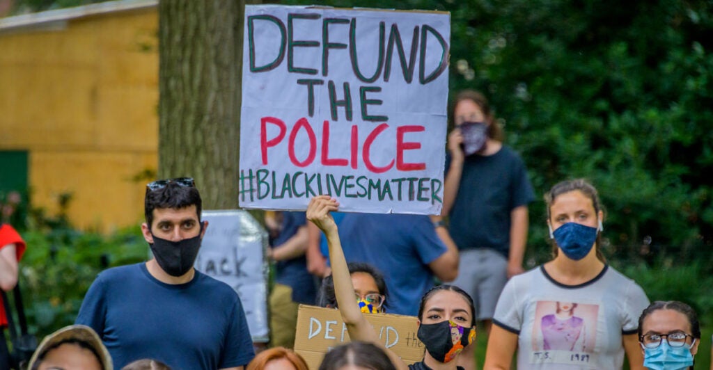 Protesters in masks hold up defund the police, Black lives matter banners