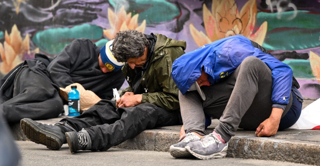 Homeless people are seen hunched over and passed out on a curb overdosed on fentanyl