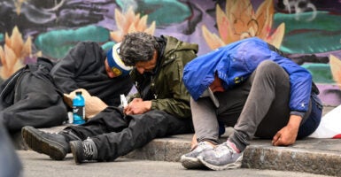 Homeless people are seen hunched over and passed out on a curb overdosed on fentanyl