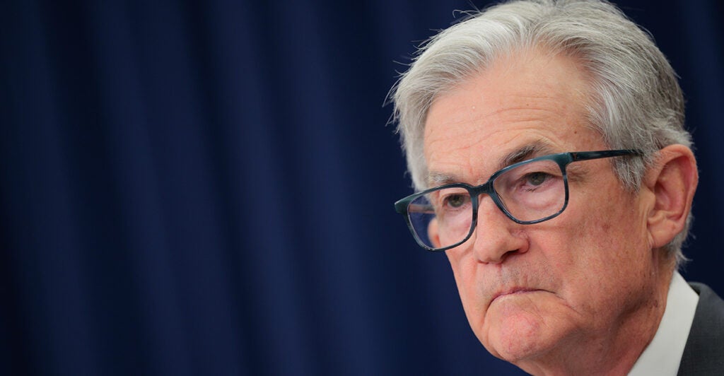 A three-quarters profile shot of Jerome Powell against a dark blue background.