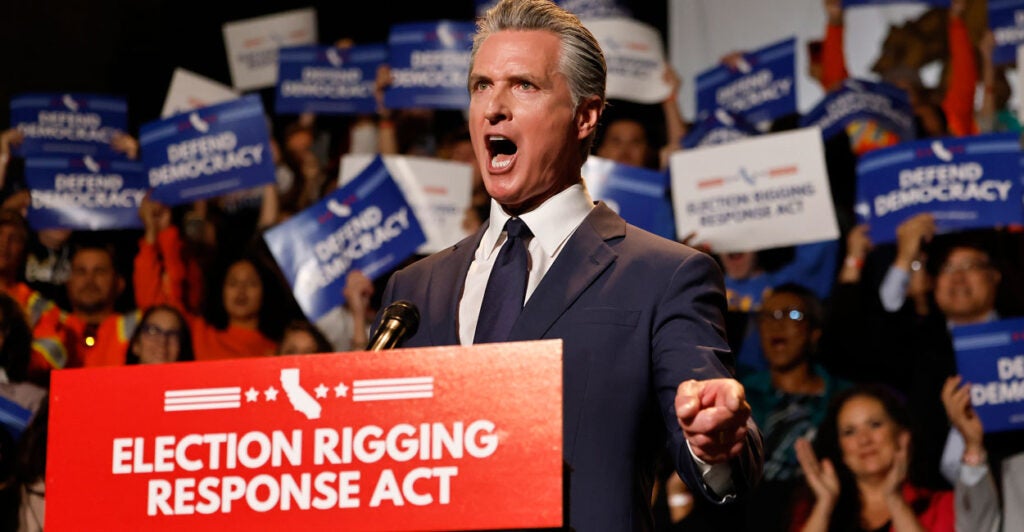 Gov. Gavin Newsom shouts at a rally at a podium with a poster for the "Election Rigging Response Act"