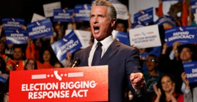 Gov. Gavin Newsom shouts at a rally at a podium with a poster for the "Election Rigging Response Act"