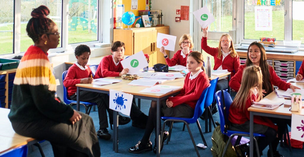 An elementary school class with children sitting around tables participating in classroom discussion wearing red sweaters