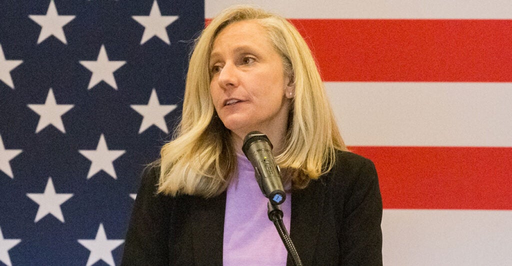 Abigail spanberger speaks at a microphone standing in front of a large American flag