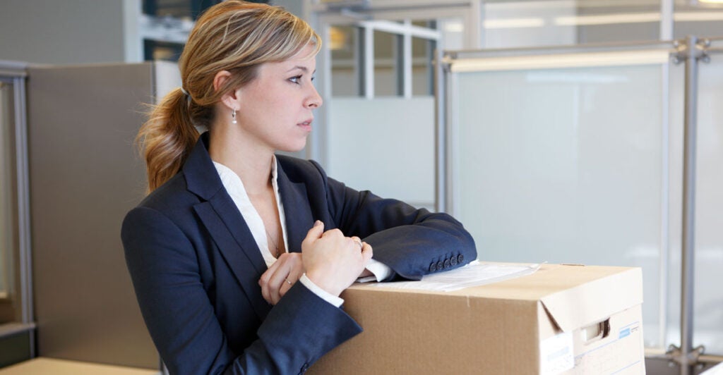 A young woman in a business suit packs up her office in in empty office suite