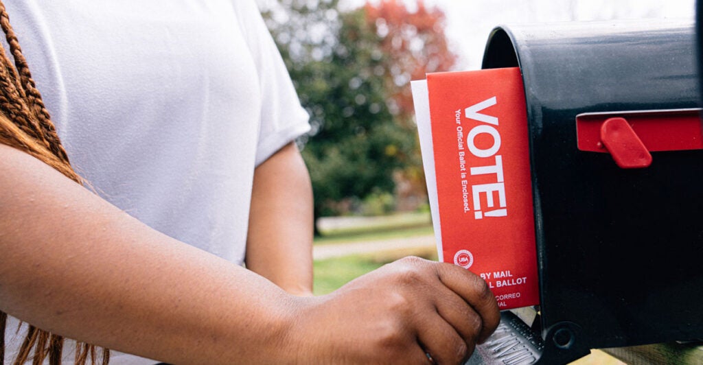 A woman puts a mail-in ballot in her mailbox to send