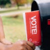 A person pulling a mail-in ballot from her roadside mailbox