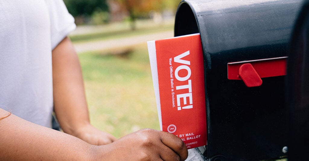 A person pulling a mail-in ballot from her roadside mailbox