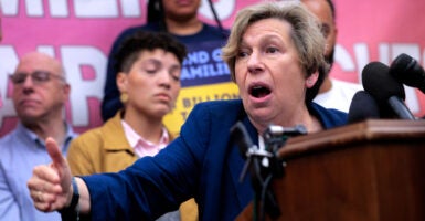 American Federation of Teachers President Randi Weingarten at a podium with multiple microphones speaking at a rally with rally goers behind her