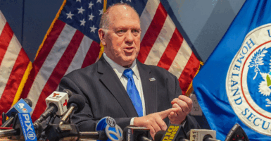 Tom Homan speaks at a podium with large American flags behind him