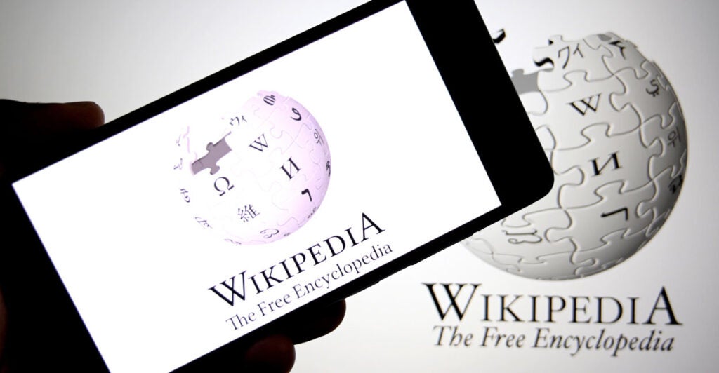 In a photo illustration, the Wikipedia logo is seen displayed on a smartphone and in the background.