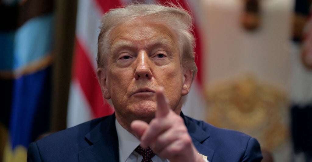 Donald Trump looks straight ahead and points with his left hand.