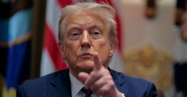 Donald Trump looks straight ahead and points with his left hand.