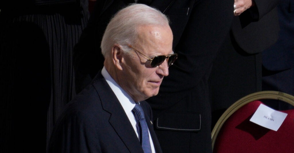 Joe Biden stands at a funeral while wearing his sun glasses.