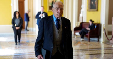 Chuck Grassley stands in a hallway with a folder in his right hand.