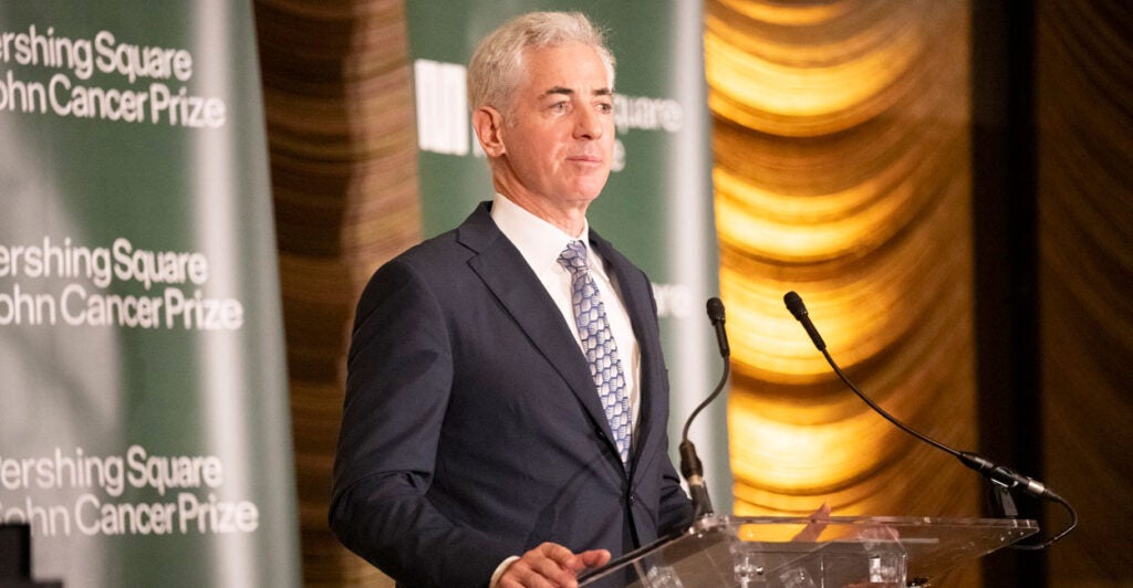 Bill Ackman stands before microphones with his hands on a podium as he looks out straight ahead.