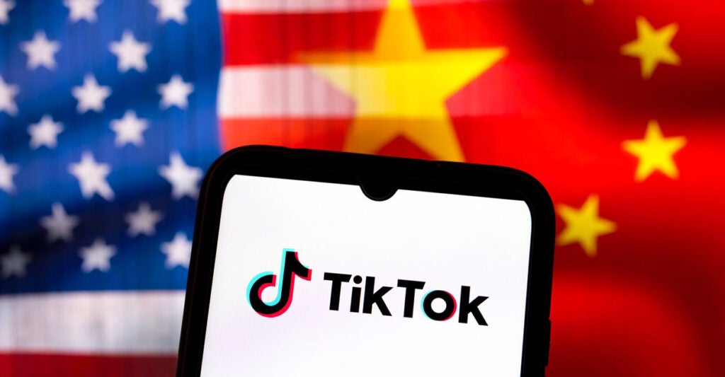 The TikTok log appears on a smartphone screen with the U.S. and Chinese flags in the background.