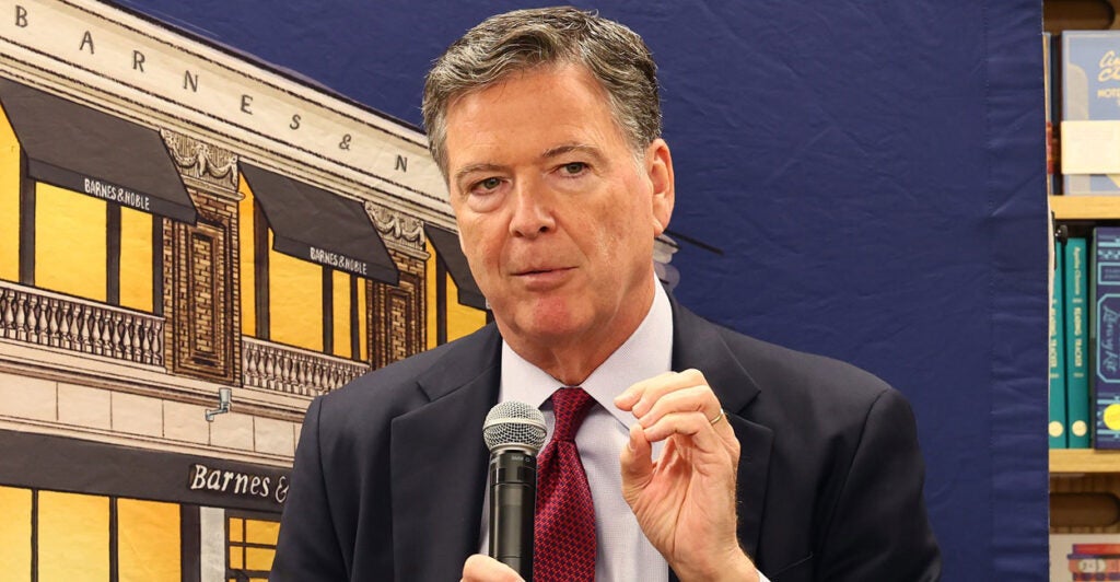 James Comey talks with a microphone in his right hand while gesturing with his left hand.