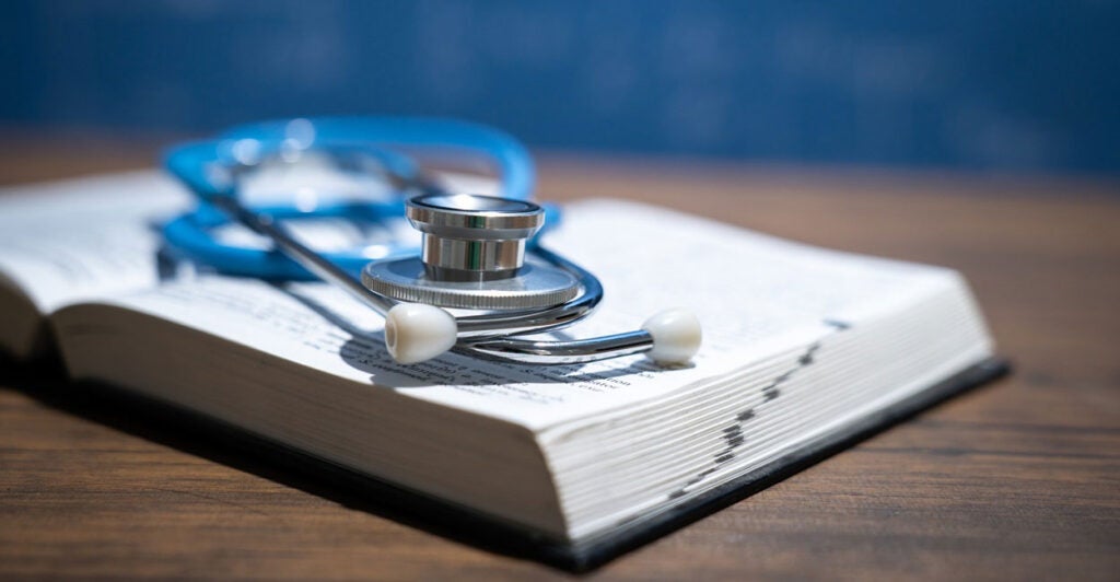 A stethoscope lays on top of an open text book on a table.
