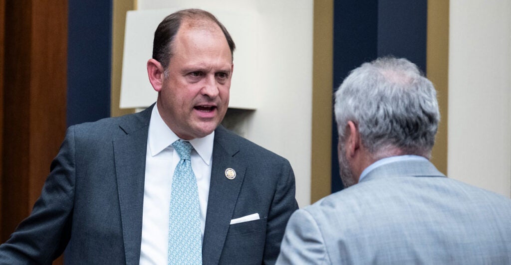 Rep. Andy Barr, R-Ky., speaks with Rep. Warren Davidson, R-Ohio, before a hearing. Both men are standing and Barr has a dark suit on and Davidson has a light grey suit on.