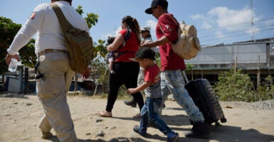 A family of migrants is seen walking outside in Mexico. One is holding a baby, and another holds the hand of a young boy and pulls a suitcase with his other hand.