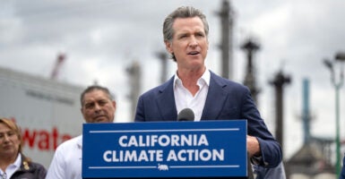Gavin Newsom, in a blue jacket and white, open-collar shirt, stands at a blue podium with white lettering, reading "California Climate Action."
