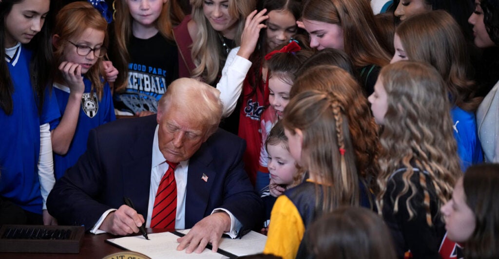 Donald Trump signs an executive order surrounded by young female athletes.