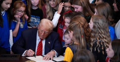 Donald Trump signs an executive order surrounded by young female athletes.