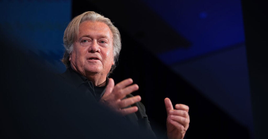 Stephen K. Bannon in black shirt against a dark background, gestures with his hands.