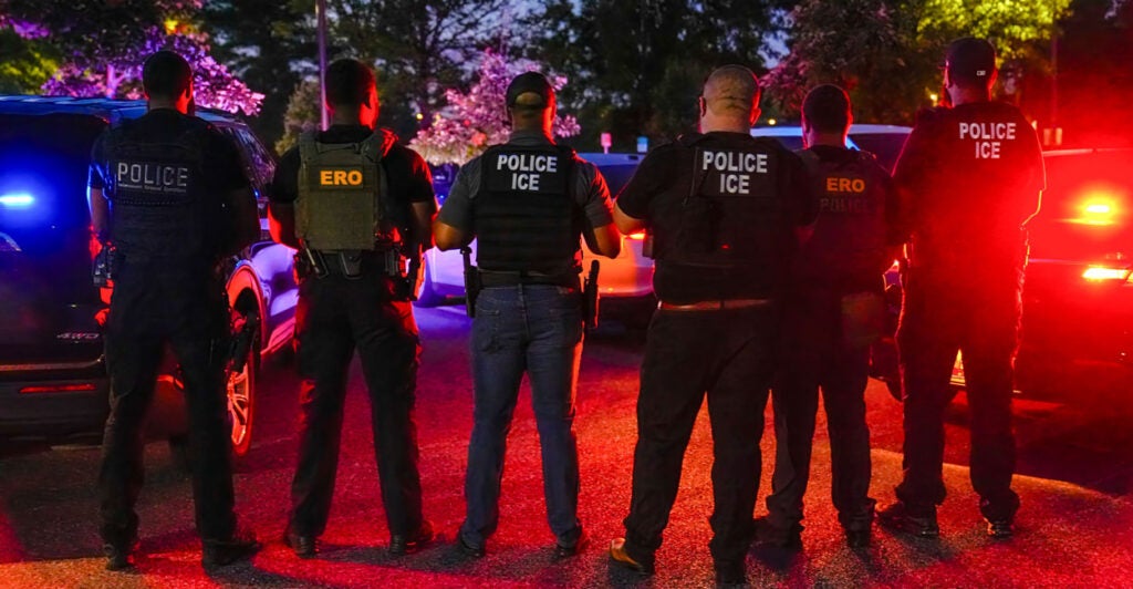 Seven ICE and ERO agents stand in a line with their backs to the camera.