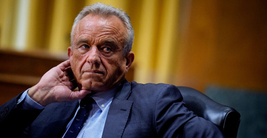 Robert F. Kennedy Jr. sits in a Senate hearing, with his hand at his cheek.