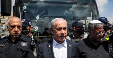 Israeli Prime Minister Benjamin Netanyahu and National Security Minister Itamar Ben-Gvir stand surrounded by law enforcement at the scene of the terrorist attack. A bus with bullet holes through the glass can be seen behind them.