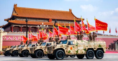 A line of Chinese-flag bearing military vehicles roll through Tiananmen Square.