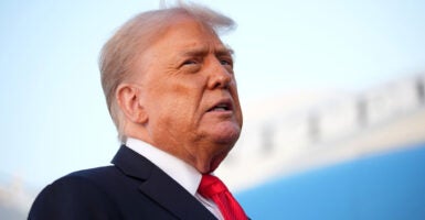 President Donald Trump looks to one side outdoors while wearing a dark suit and red tie.