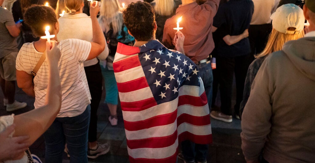 A young man wrapped in American flag is among a crowd gathered for a candlelight vigil honoring Charlie Kirk.