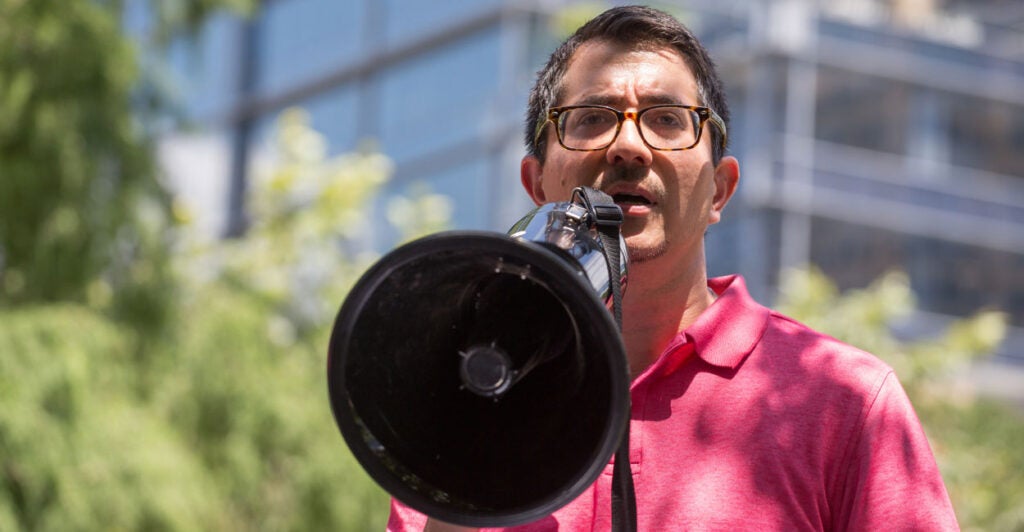 Jose Garza in a pink shirt speaks into a megaphone.