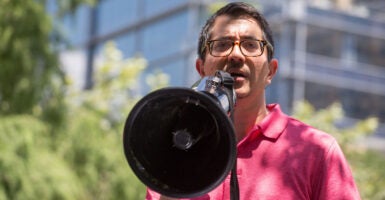 Jose Garza in a pink shirt speaks into a megaphone.