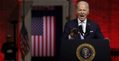 Joe Biden, on a blood red-lit stage, with an American flag and Marine behind him angrily speaks.